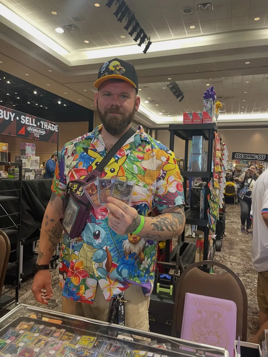 A collector in a Pokémon shirt holding up three cards he picked up