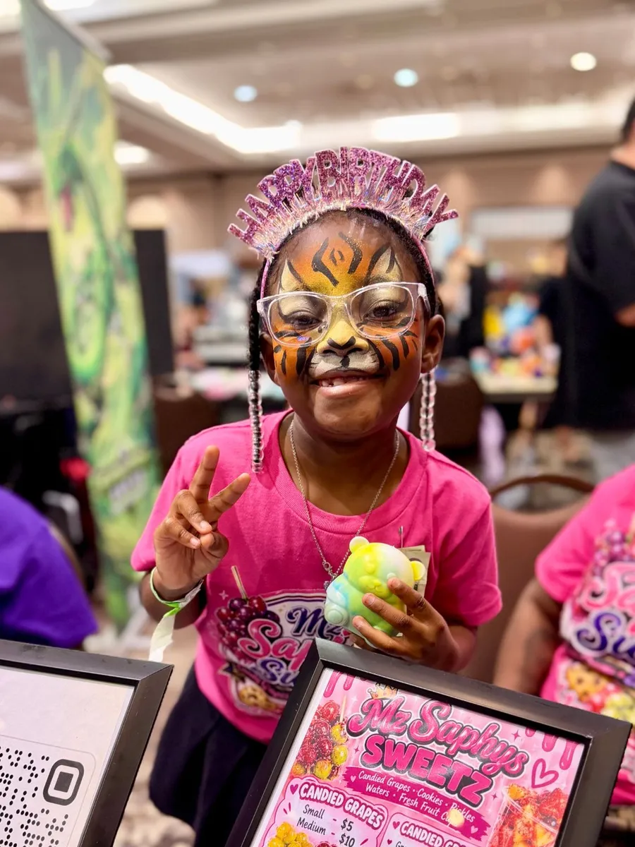 A smiling birthday girl with tiger face paint at a vendor booth
