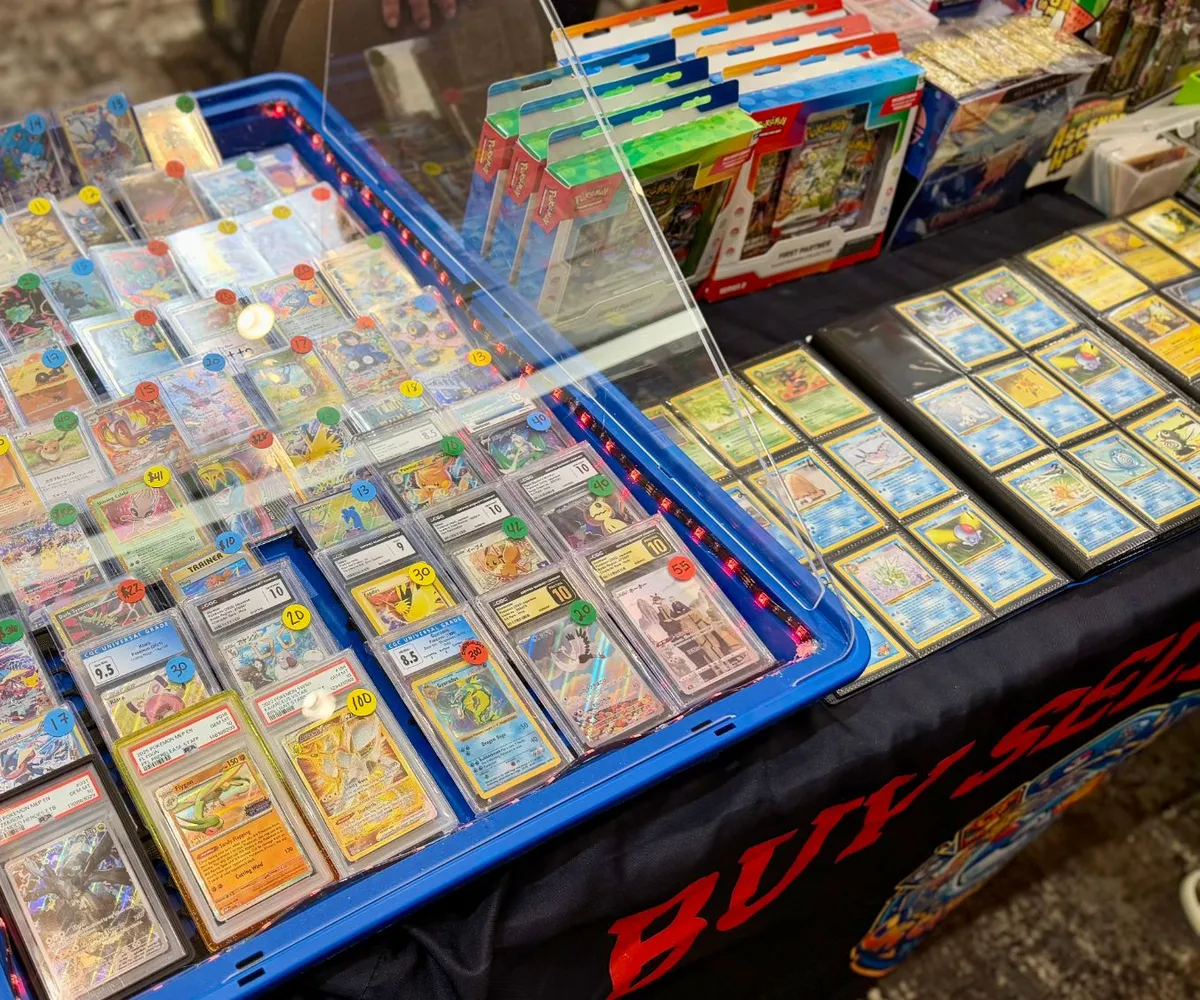 A vendor's case of graded Pokémon cards beside a Buy, Sell, Trade banner